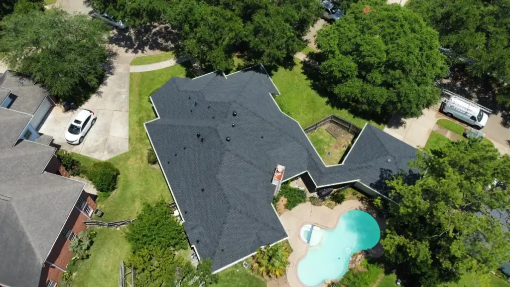 Overhead drone view of a dark gray shingle roof with multiple gables above a backyard swimming pool in Cypress, TX