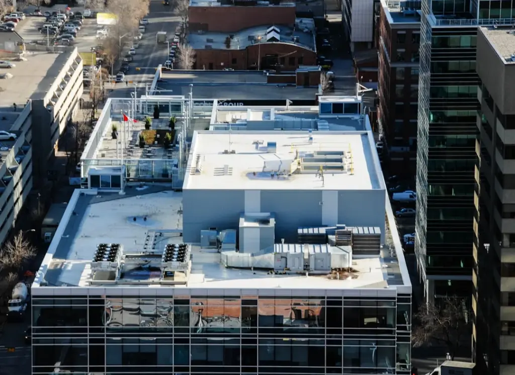 Aerial view of a flat commercial building roof with rooftop HVAC units, ductwork, and a rooftop patio area in a downtown