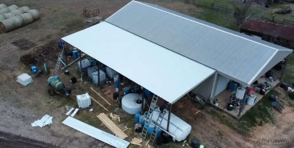 Aerial view of an open-sided metal roof storage structure with farm equipment and containers underneath, Cypress, TX