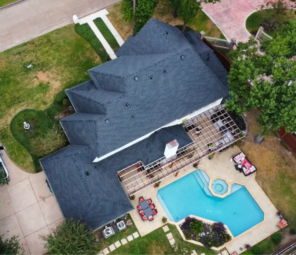 Aerial photo of a gray shingle roof with stepped gables above a backyard pool, spa, and pergola in Cypress, TX