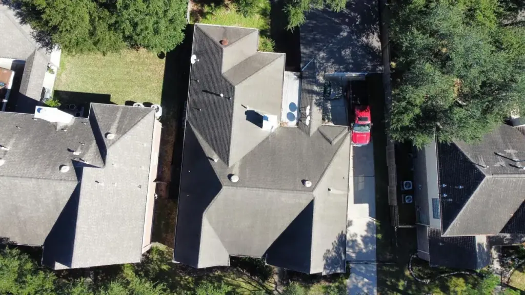 Aerial view of a multi-level shingle roof between neighboring homes with a red truck parked in the driveway in Cypress, TX