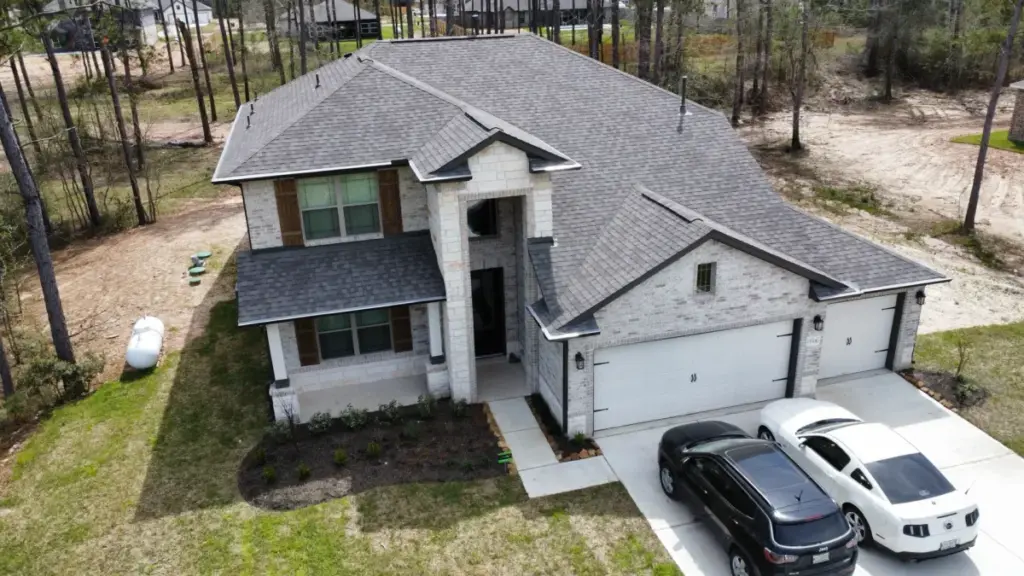 Aerial view of a gray shingle roof on a two-story brick home with a wooded lot in Cypress, TX