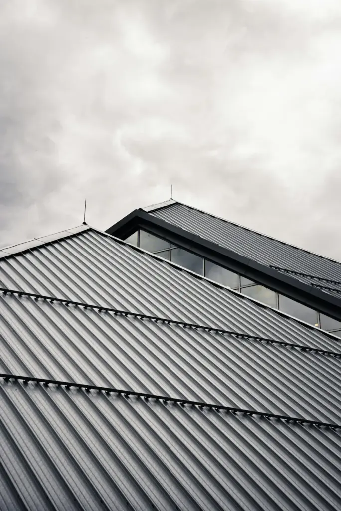 Low angle view of a corrugated metal roof peak with clerestory windows under a cloudy sky in Cypress, TX