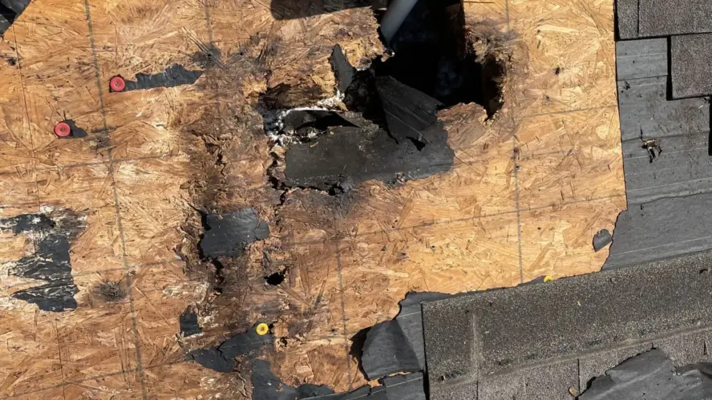 Close-up of exposed plywood roof decking with torn shingles and old shingle debris during a roof replacement
