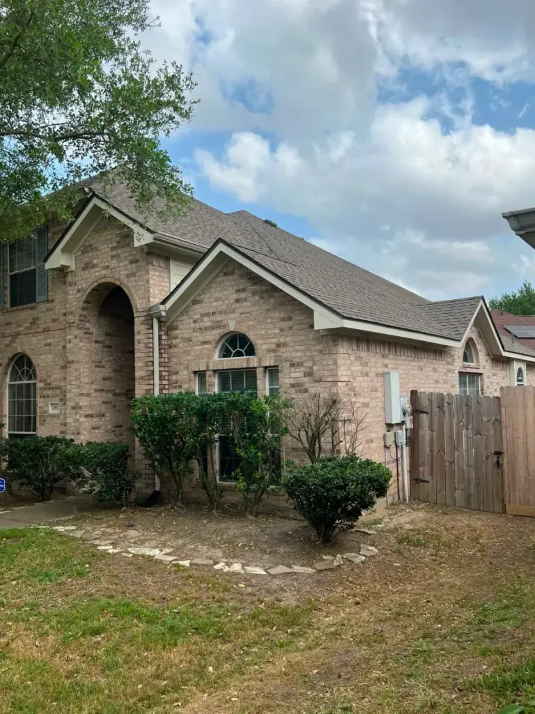 Brick home with arched entryway and multiple asphalt shingle roof gables, wood fence gate to the side