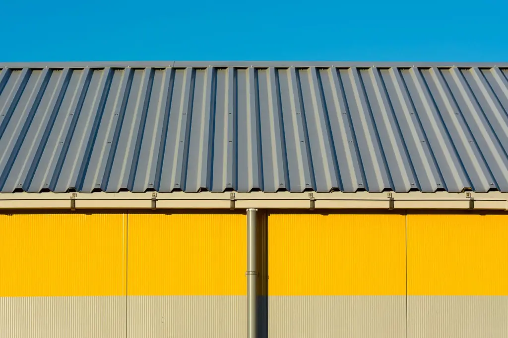 Gray corrugated metal roof edge with gutter above a yellow and beige corrugated metal wall