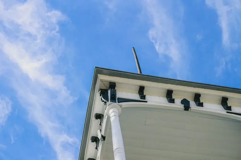 Low angle view of a white porch roofline with decorative brackets and a metal roof edge against a blue sky