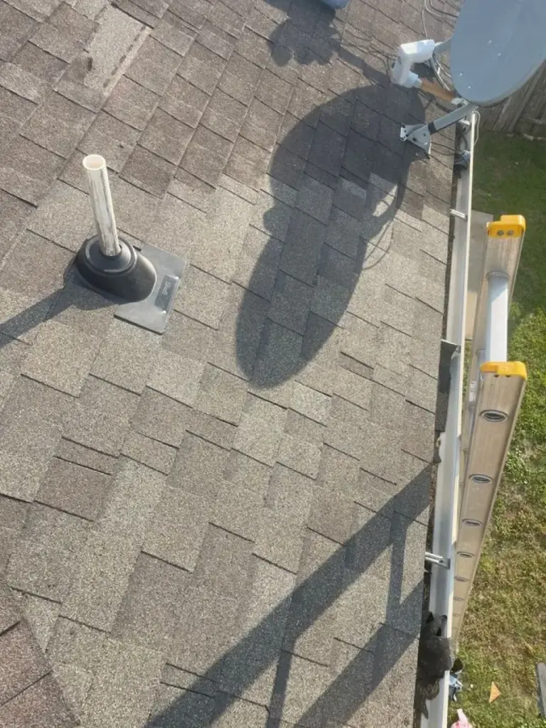 Close-up view of shingle roof with pipe vent boot, satellite dish mount, and ladder along the edge in Cypress, TX