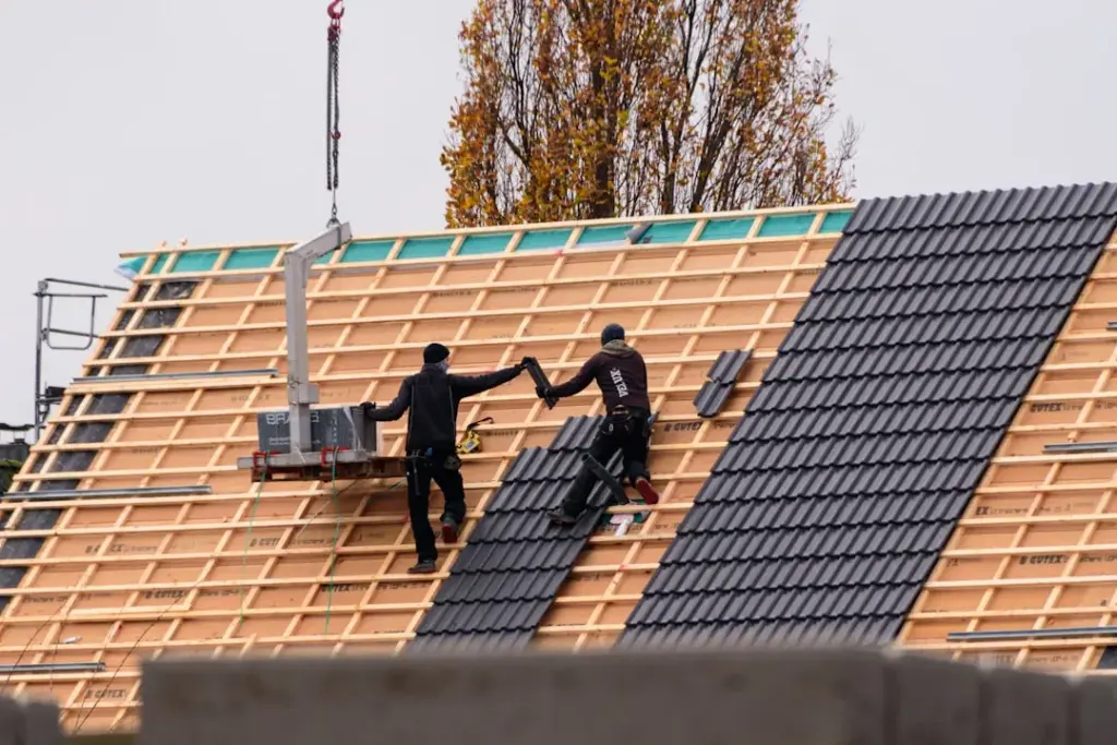 Two roofers on a steep batten lath roof passing a roof tile during installation