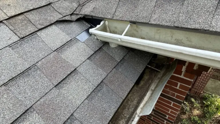 Close-up of a gray shingle roof valley meeting a white gutter above a brick wall on a Cypress, TX home