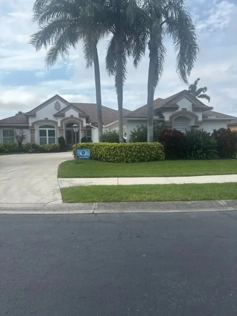 Street view of a single-story stucco home with a tile roof, arched entry, and tall palm trees in the front yard