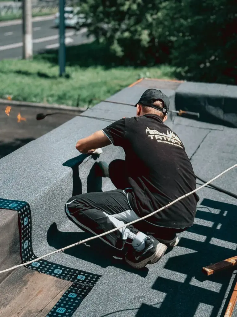 Roofer kneeling on a flat roof using a propane torch to seal membrane seams